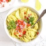 pasta guacamole in a white bowl sprinkled with tomatoes and onions