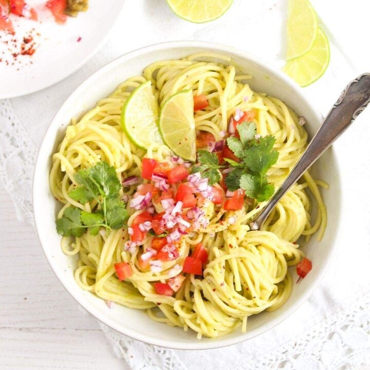 pasta guacamole in a white bowl sprinkled with tomatoes and onions