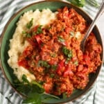 Hungarian lecso with eggs and peppers served with mash in a bowl with a spoon in it.