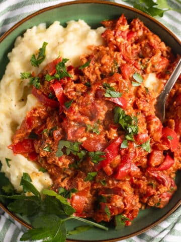 Hungarian lecso with eggs and peppers served with mash in a bowl with a spoon in it.