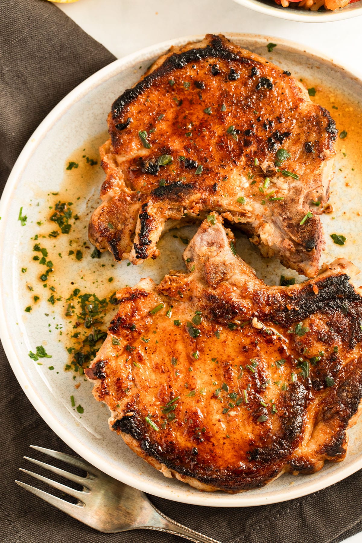two milk marinated pork chops and their cooking juices on a plate.