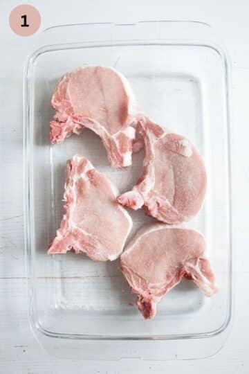 four seasoned raw pork chops on a cutting board.