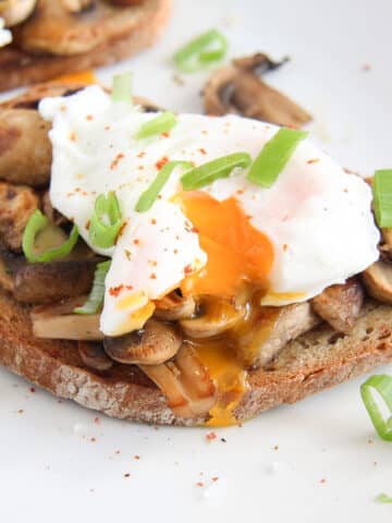 mushroom toast with poached egg on top sprinkled with green onions and pepper.