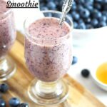 glass of smoothie with a bowl of blueberries behind