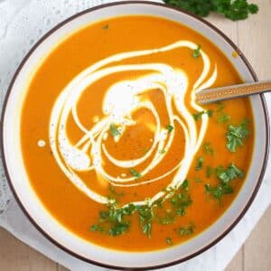 bowl of pumpkin and sweet potato soup drizzled with coconut cream and parsley.