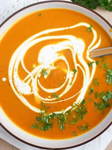 bowl of pumpkin and sweet potato soup drizzled with coconut cream and parsley.