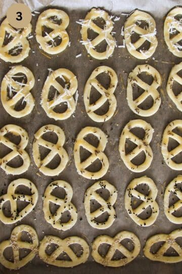 unbaked covrigei sprinkled with caraways seeds, sesame, and cheese on a baking sheet.