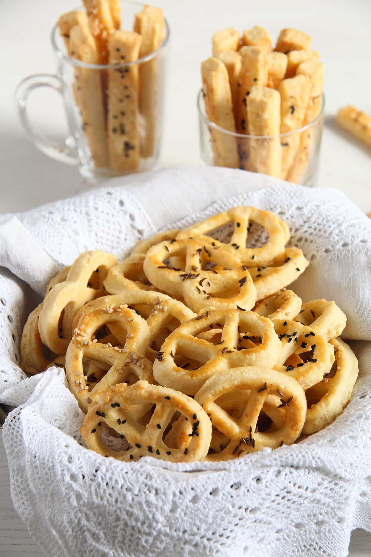 romanian pretzels or covrigei in a bowl lined with a towel and some more cheese sticks behind them.