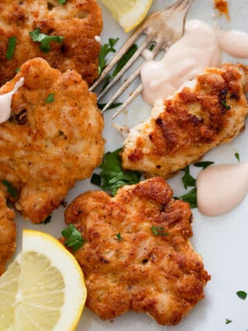 russian chicken patties, lemon wedges, dip and a fork on a plate.