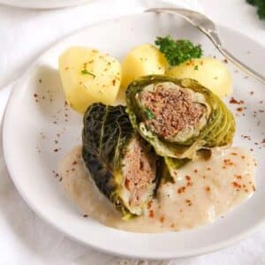 stuffed savoy cabbage rolls with potatoes and sauce on a plate.