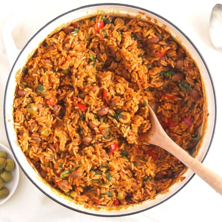 spanish rice and beans with olives and peppers in a white pot.