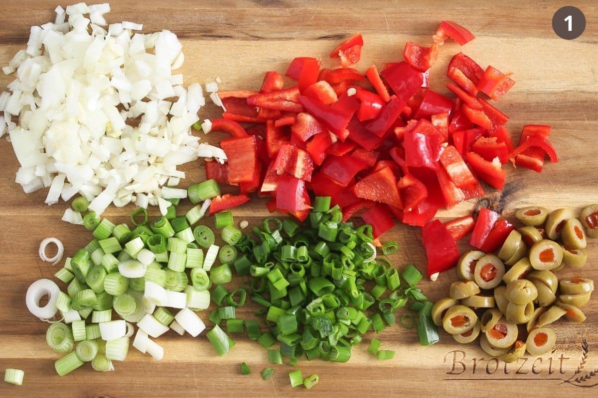chopped onions, peppers, green onions and olives on a wooden board.