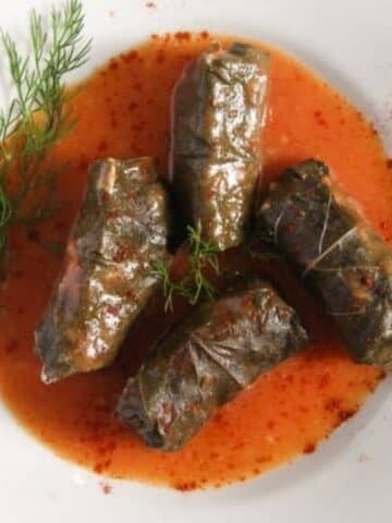 four rolls of grape leaves in a plate with sauce.