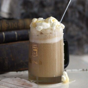 boozy butterbeer topped with whipped cream and butterscotch syrup in a mug.