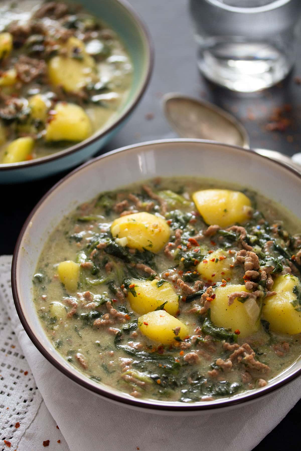 two bowls of beef, potato and spinach curry and a glass of water.