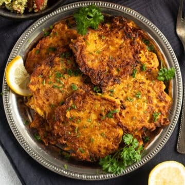 many butternut squash fritters on a silver plate with parsley and lemon slices.