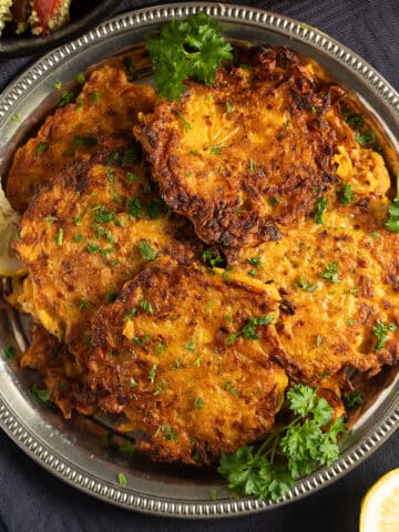 many butternut squash fritters on a silver plate with parsley and lemon slices.