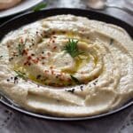 fava bean dip drizzled with olive oil and sprinkled with parsley and chili flakes in a bowl.