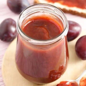 a jar full of german plum butter and a few plums behind it.