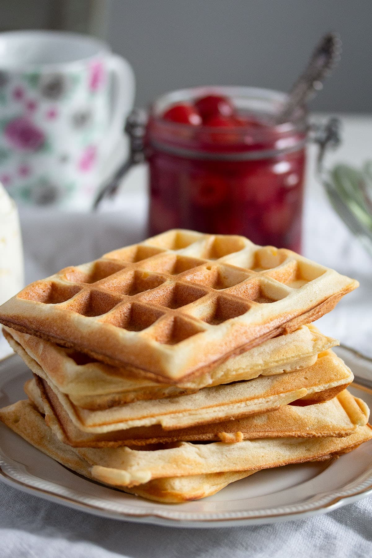 five waffles stapled on a plate and a jar of cherry sauce behind.