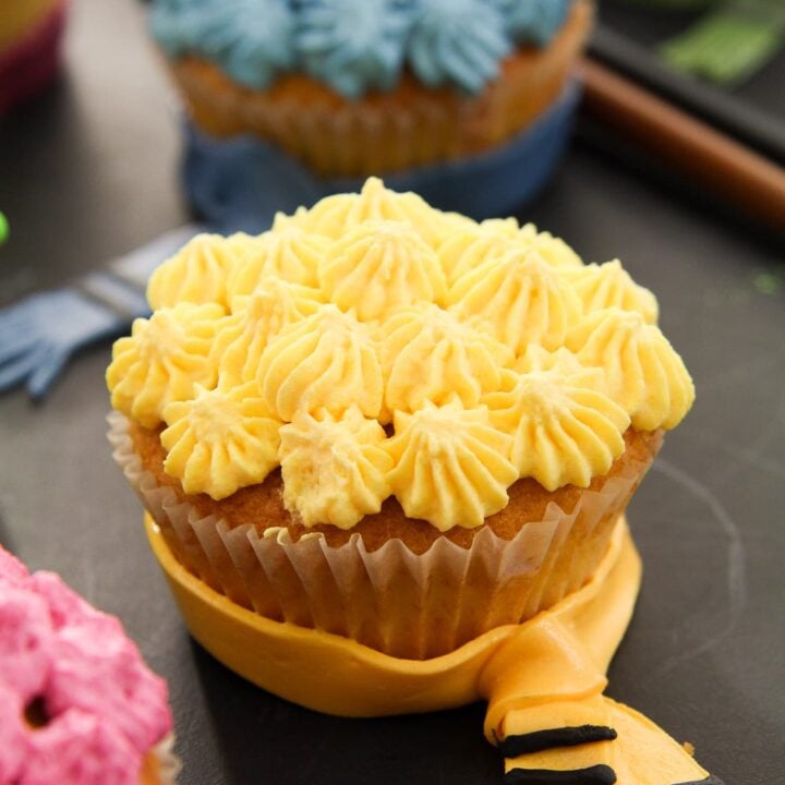 yellow hufflepuff cupcake decorated with whipped cream and a fondant scarf