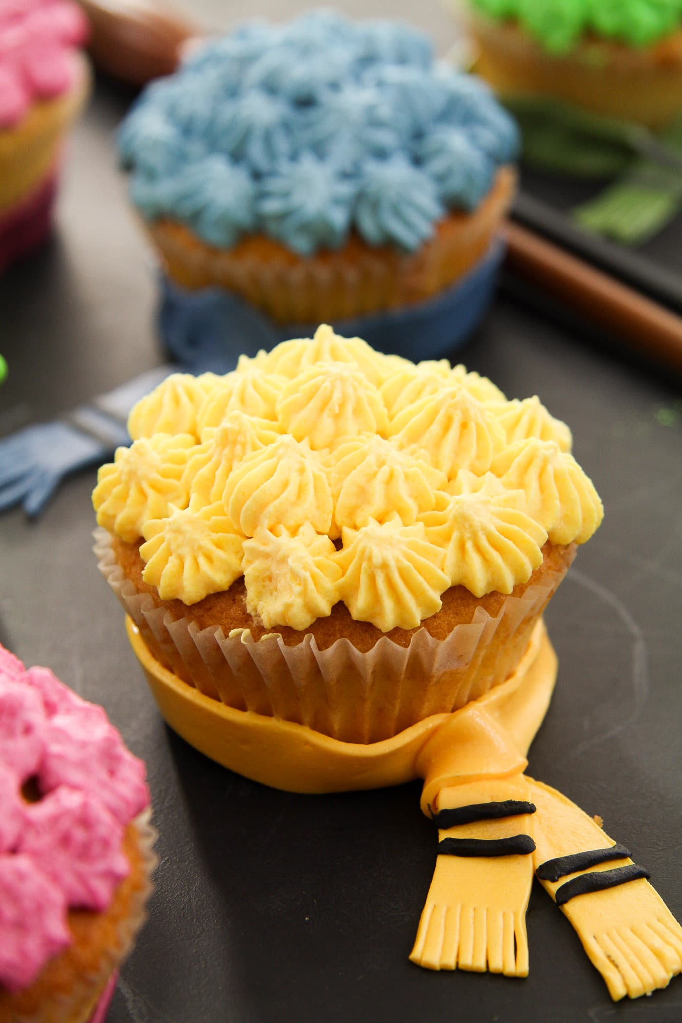 yellow hufflepuff cupcake decorated with whipped cream and a fondant scarf