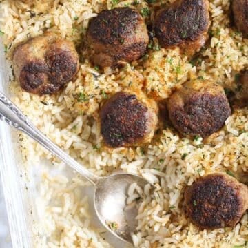 meatballs and rice being served with a spoon directly from the baking dish.
