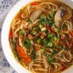 spicy mushroom noodles soup with herbs served in a white bowl.