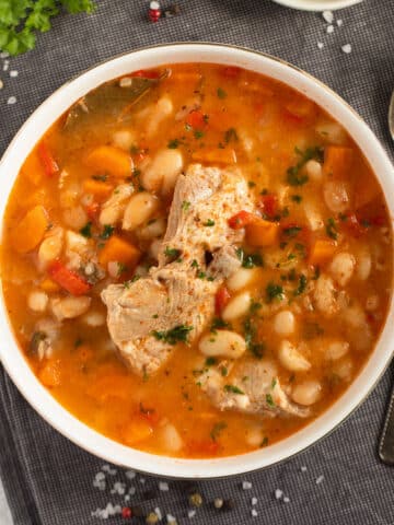 bowl of pork rib soup showing the ribs and the white beans on a grey kitchen cloth with a spoon beside it.