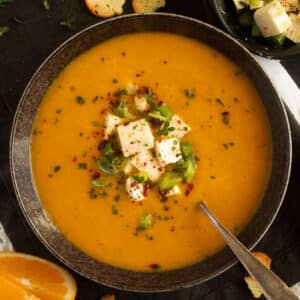 bowl of pumpkin orange soup topped with marinated feta and green onions.