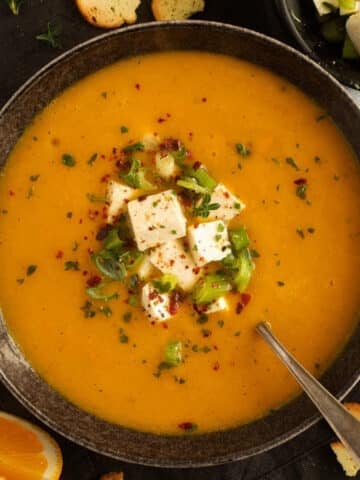 bowl of pumpkin orange soup topped with marinated feta and green onions.