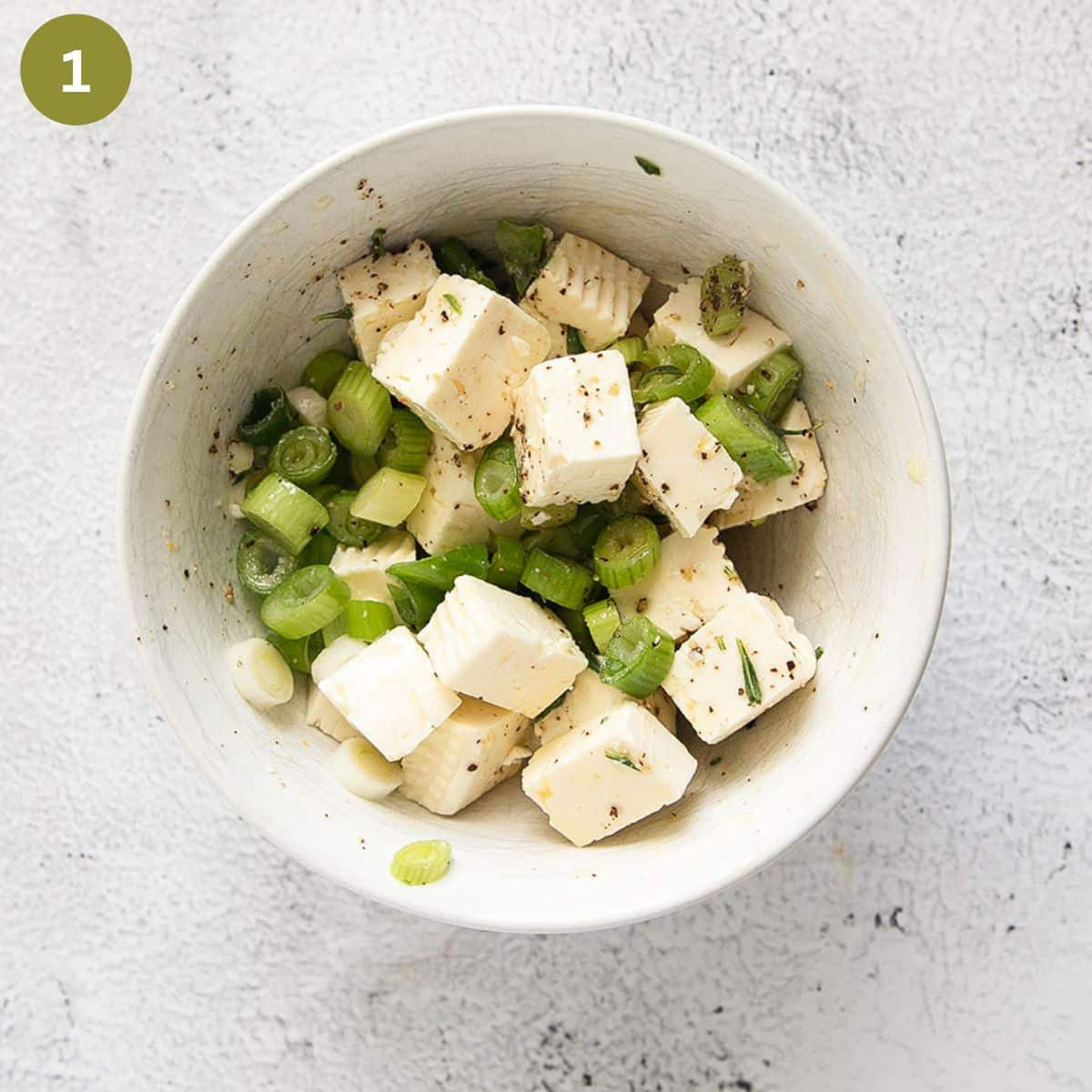 feta cubes and green onion rings marinating in a small white bowl.
