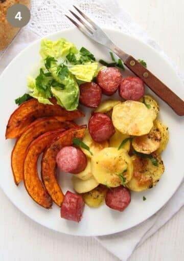 a plate with pumpkin, sausage and potato slices, a few lettuce leaves and a fork.
