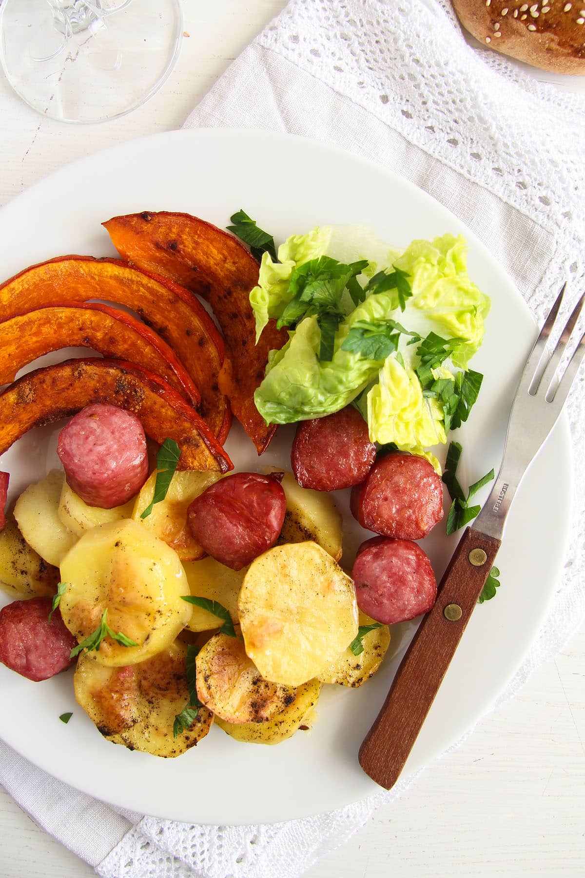 pumpkin wedges, potato slices and sausage pieces with salad leaves and a fork on a plate.