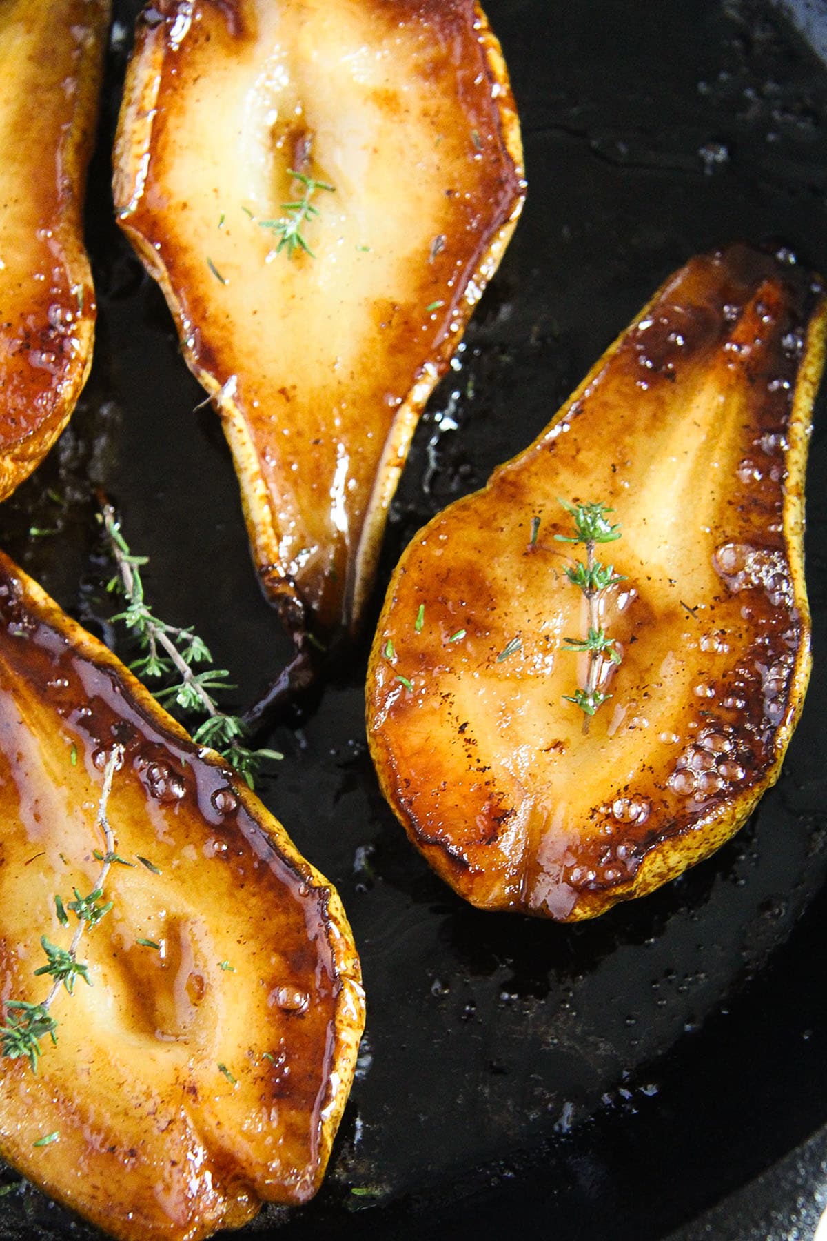 caramelized roasted pears garnished with fresh tyhme in a skillet.