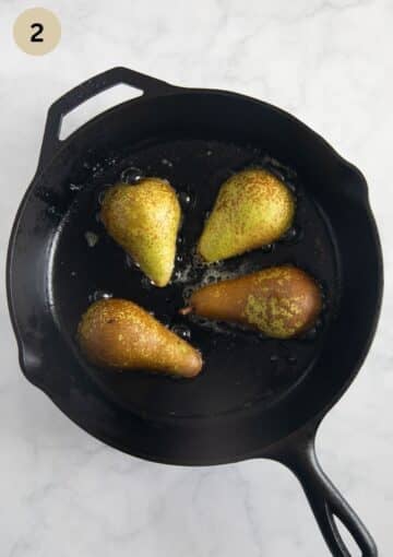 cooking four pear halves in butter in a cast iron skillet.