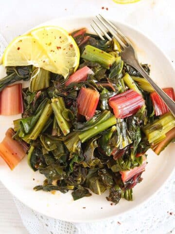 steamed swiss chard served with lemon slices on a white plate