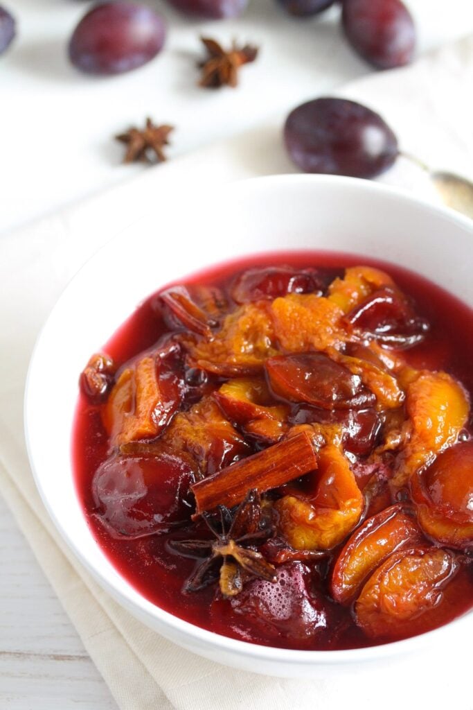 bowl of stewed plums with a cinnamon stick on top