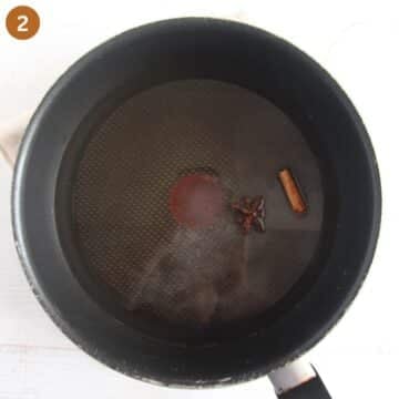 sugar and water mixture with star anise and cinnamon in a saucepan for adding to plum stew.