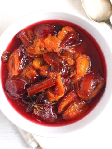 stewed plums in a small white bowl with cinnamon and star anise on top