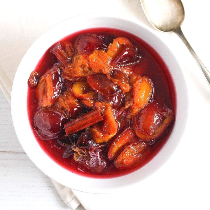stewed plums in a small white bowl with cinnamon and star anise on top