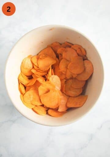 raw sweet potato slices mixed with spices and oil in a large bowl.