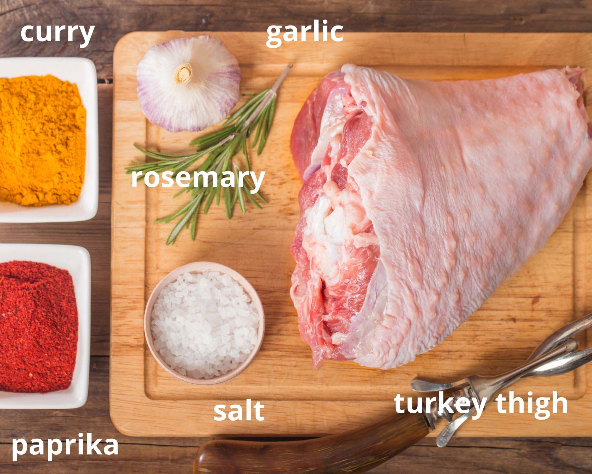 raw turkey thigh, spices, rosemary and garlic on a wooden board.