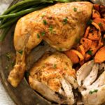 roasted chicken quarters with sweet potatoes and green beans on a platter.