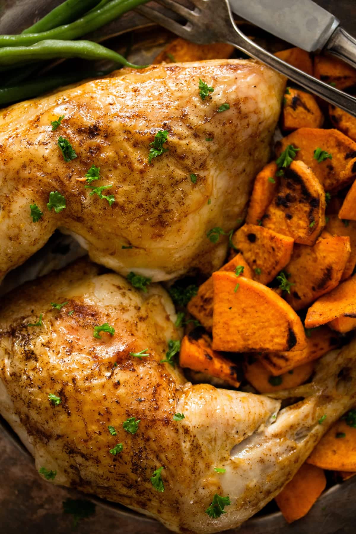 close up golden brown chicken leg quarters served with sweet potatoes.