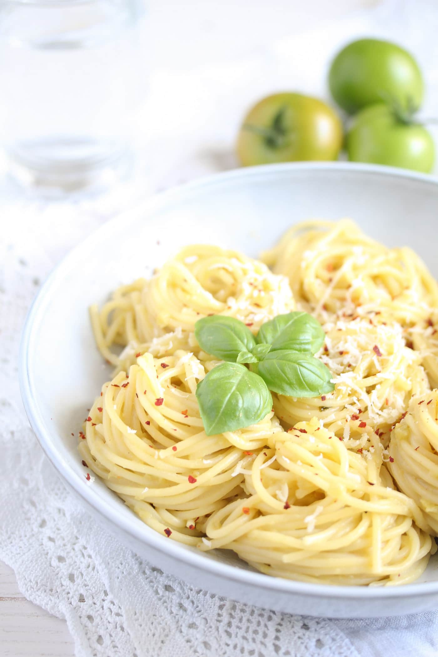 spaghetti with green tomato sauce and basil in a white bowl