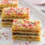 three pieces of romanian harlequin cake layered with jam and sprinkled with colorful sprinkles.