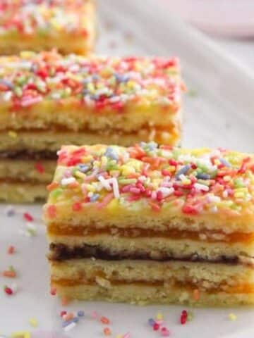 three pieces of romanian harlequin cake layered with jam and sprinkled with colorful sprinkles.