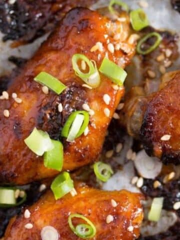 korean chicken wings with gochujang wing sauce sprinkled with green onions and sesame seeds.