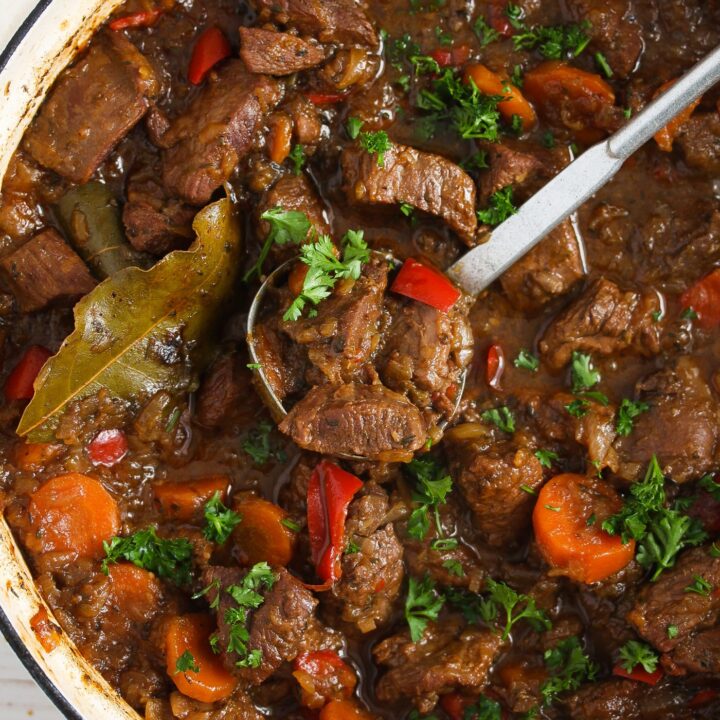 turkey stew in a white pot with onions and carrots